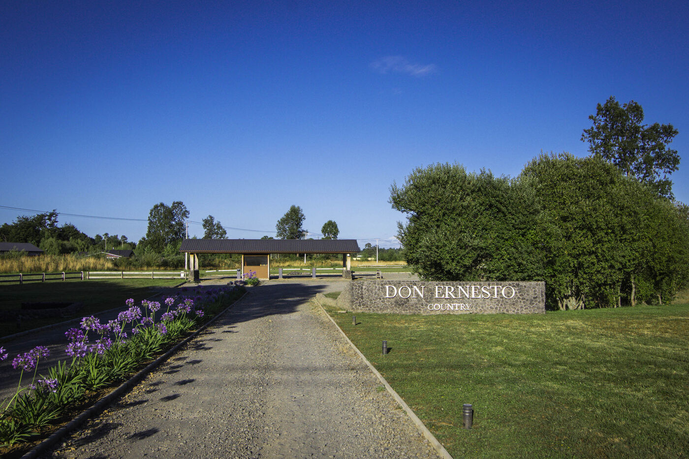 Acceso de Don Ernesto Country con camino de gravilla y flores